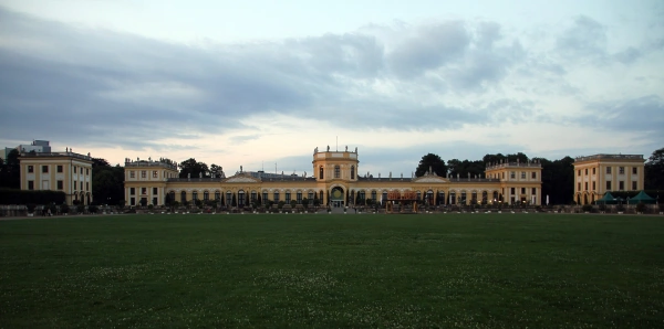 Die lange gelbe Barockfassade der Orangerie in Kassel mit ihren Pavillons, davor die weite Rasenfläche der Karlswiese in der Abenddämmerung.