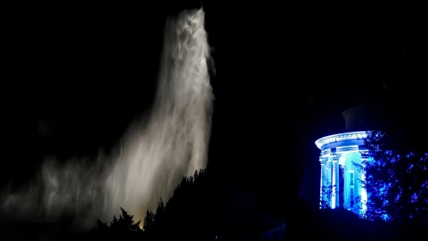 Die angestrahlte Große Fontäne bei Nacht neben einem blau beleuchteten Rundtempel im Bergpark Wilhelmshöhe.