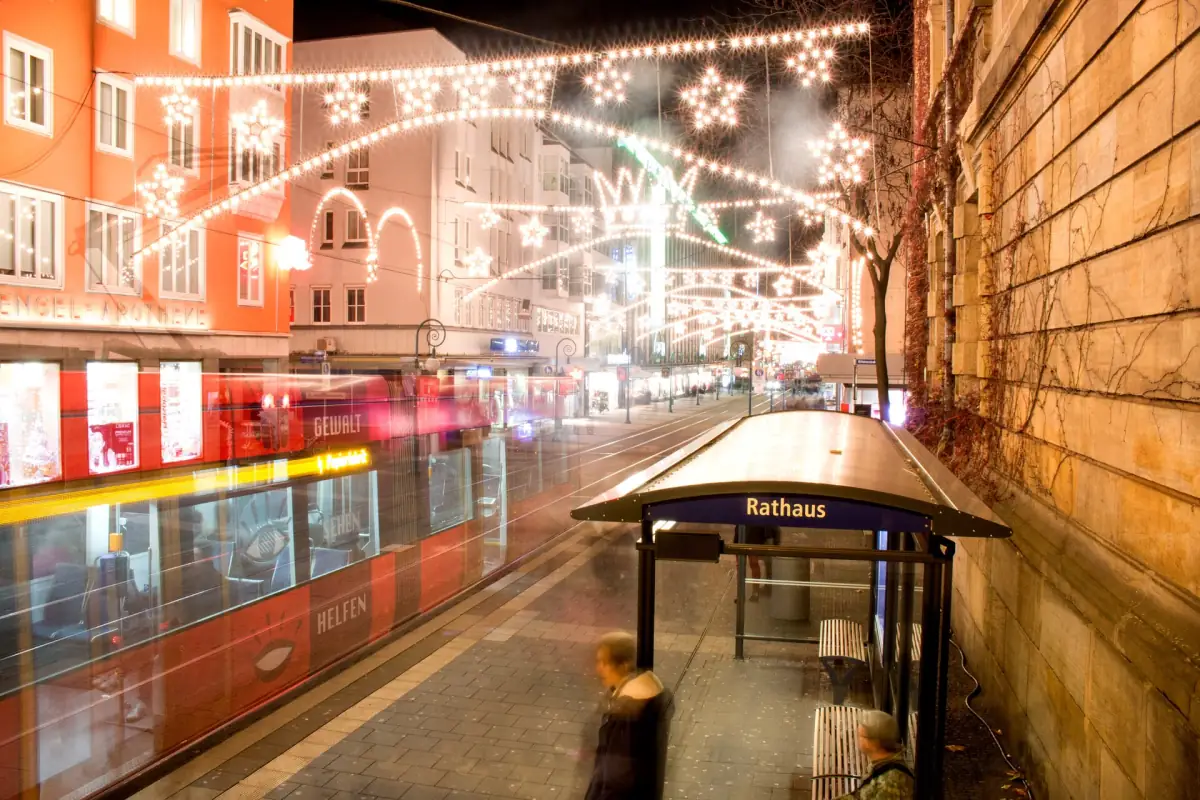 Lichterbögen und Sterne über der Oberen Königsstraße in Kassel bei Nacht, vorn die Straßenbahnhaltestelle Rathaus und eine vorbeifahrende Tram.